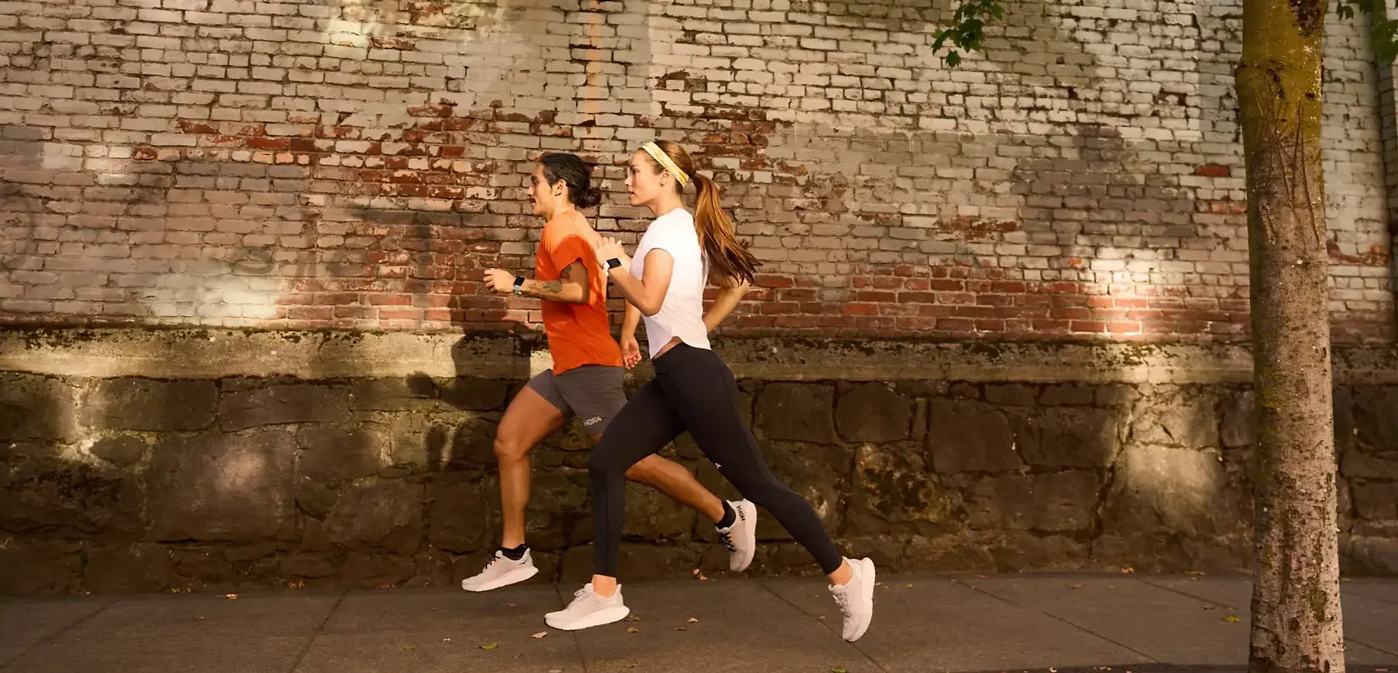 Man and woman running on a street in a pair of HOKA running shoes