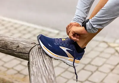 Man tying a pair of Team brooks Adrenaline GTS 23 running shoes